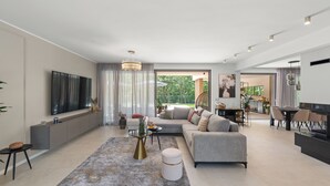 Un salon moderne doté d’un grand téléviseur à écran plat, d’un canapé gris, d’une table basse et d’un coin repas avec une table et des chaises.