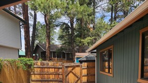 Un patio trasero con un sendero de grava que lleva a un portón de madera, rodeado de árboles y una casa con fachada verde.