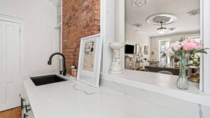 Eine Küche mit weißem Marmorarbeitsplatz, einem schwarzen Wasserhahn, einer Ziegelwand und einem gerahmten Bild.
