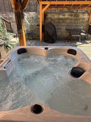 A hot tub with a wooden pergola overhead, surrounded by a brick wall and potted plants.
