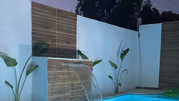 A rectangular swimming pool with a waterfall feature, surrounded by a white wall and a wooden fence. - Yasmine Hammamet, villa with pool near Carthage Land. (Yasmine Hammamet)