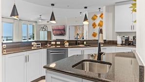 A modern kitchen with white cabinets, a granite countertop, and black pendant lighting.