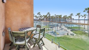 A balcony with a table and chairs, overlooking a pool area with palm trees and a clear sky.