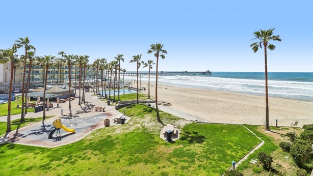 A beachside hotel with a pool, palm trees, and a pier in the background.