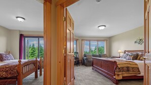 A bedroom with two wooden beds, a sofa, a chair, and a view of trees through large windows.