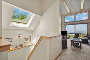 A spacious living area with a high ceiling, a skylight, a balcony with a view, and a flat-screen TV.
