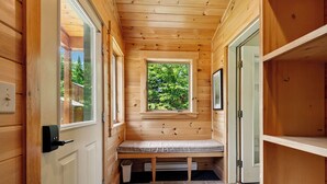 A wooden cabin interior with a bench, a window with a view of trees, and a door.