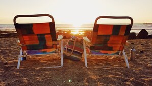 Deux chaises de plage, recouvertes d’une couverture colorée, sur une plage de sable au coucher du soleil.