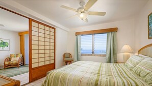 Une chambre à coucher avec un lit, un ventilateur de plafond, une fenêtre avec des rideaux, une chaise et une porte coulissante en bois.