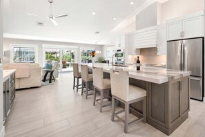 Cozinha moderna com ilha central, eletrodomésticos de aço inoxidável e área de refeições com sofá e cadeiras.