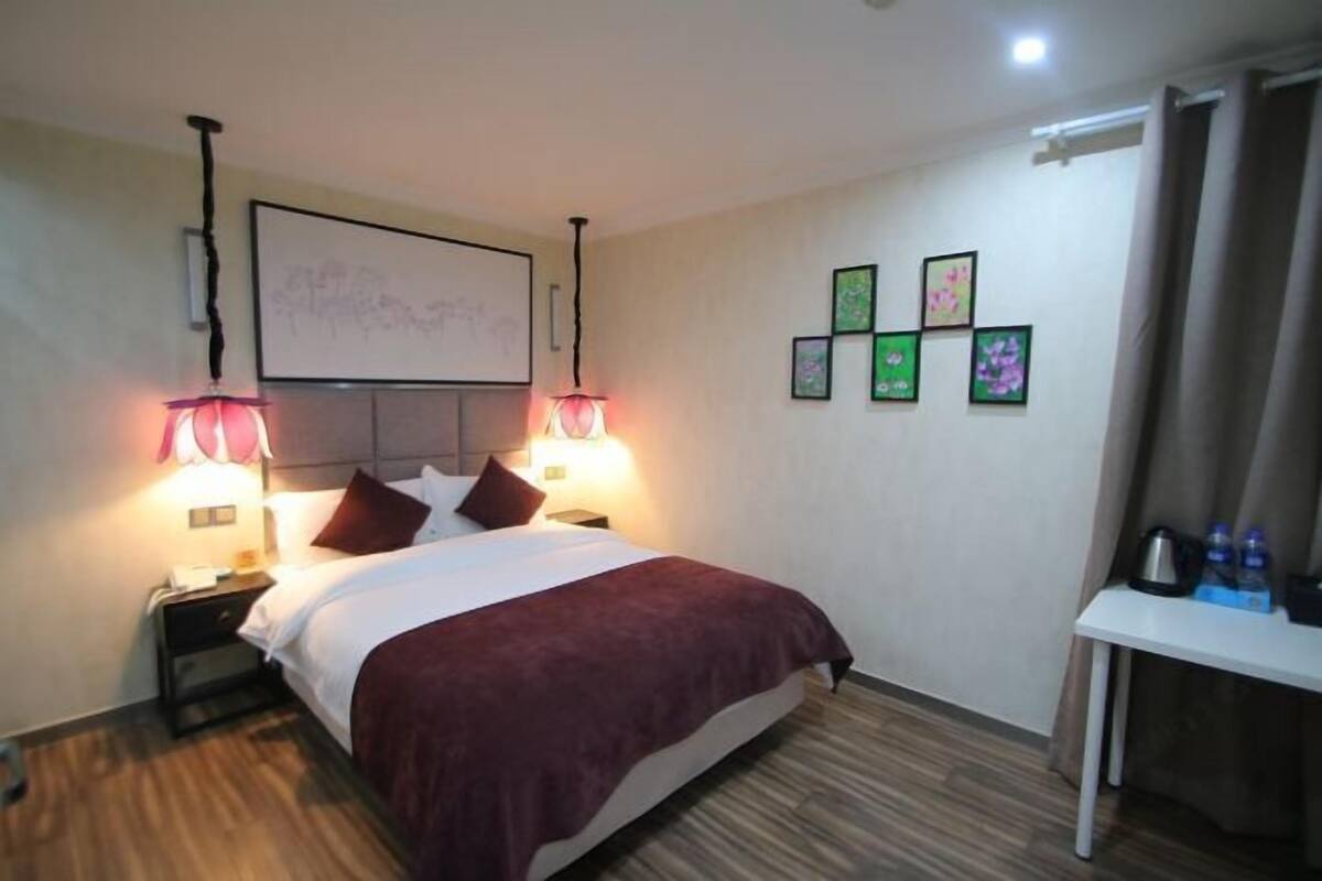 Une chambre d’hôtel avec un lit, deux lampes de chevet, une table de chevet, une petite table avec des bouteilles d’eau et un mur orné de tableaux.