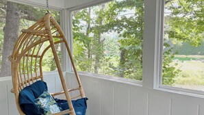 A wicker swing chair with blue cushions in a room with large windows overlooking a green landscape.