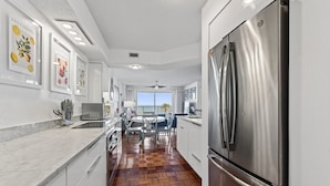 Une cuisine moderne avec des meubles blancs, un réfrigérateur en acier inoxydable et un parquet en bois disposé en chevrons.