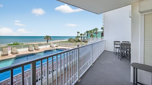 Un balcon avec une piscine, des chaises et une table, offrant une vue sur la plage et l’océan.