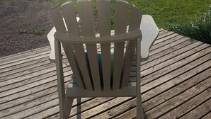 A wooden deck with a white Adirondack chair facing a grassy field.