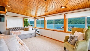 Un dormitorio con cama, sofá, sillón y ventanas amplias con vista al lago.
