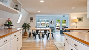 Una cocina moderna con muebles blancos, encimera de madera y una zona de comedor con sillas.
