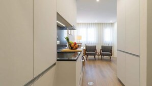 A modern kitchen with a central island, a dining area with two chairs, and a view of a window with curtains.
