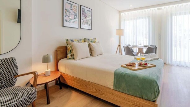 A hotel room with a bed, a chair, a small table with a lamp, a breakfast tray, and two framed pictures on the wall.