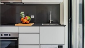 A modern kitchen with white cabinetry, a black countertop, a fruit bowl, a stainless steel range hood, a built-in oven, and a dishwasher.