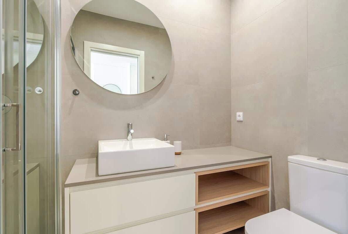 A modern bathroom with a round mirror, a white sink, and a toilet.