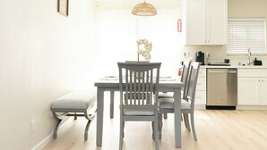 A modern kitchen with white cabinets, a built-in dishwasher, and a dining area with a table and chairs.