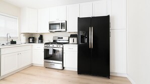 A modern kitchen with white cabinets, a black refrigerator, a microwave, a stove, and a coffee maker.