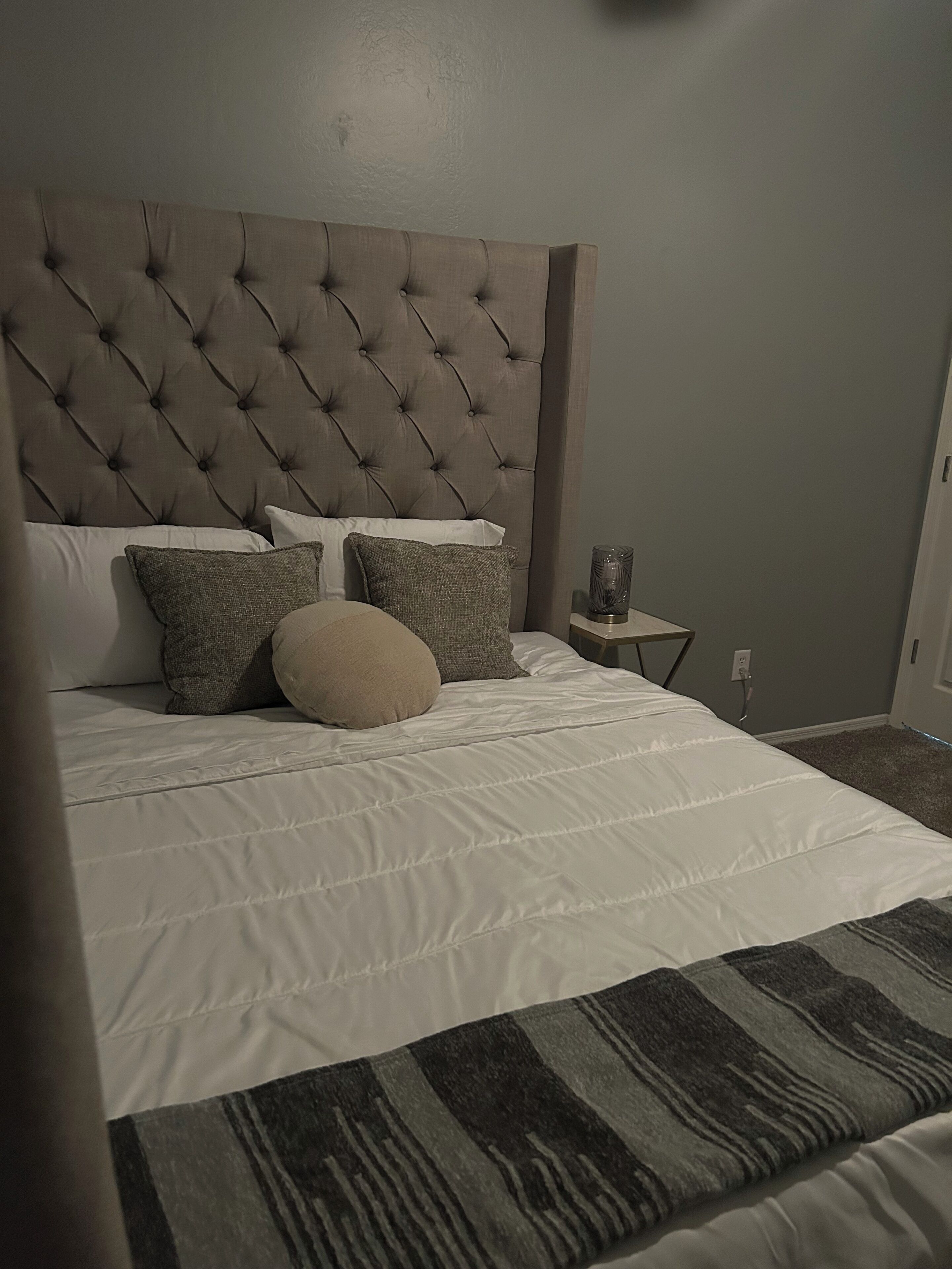 A neatly made bed with a tufted headboard, white bedding, and several pillows.