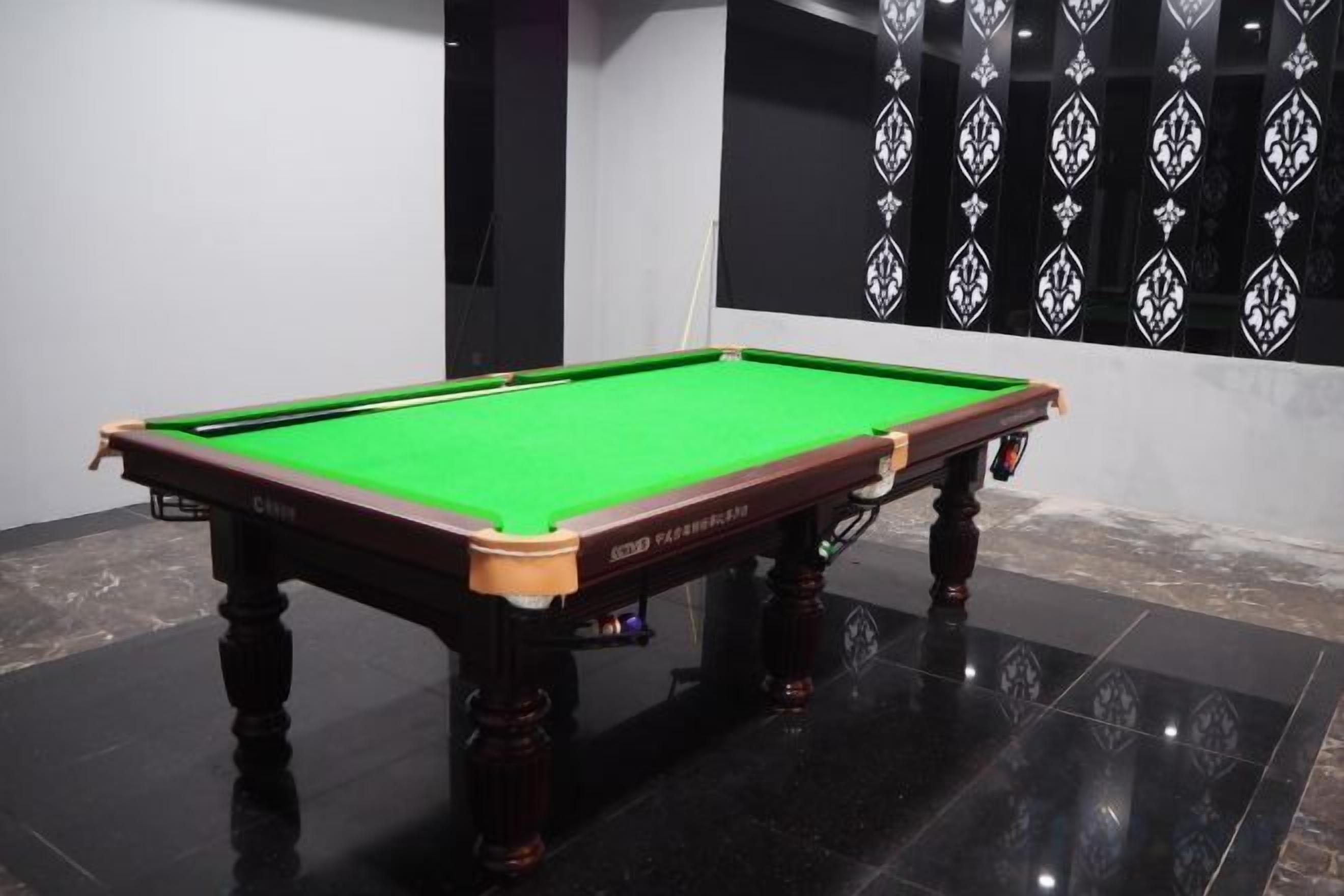 A pool table with a green felt surface, positioned on a glossy black floor.