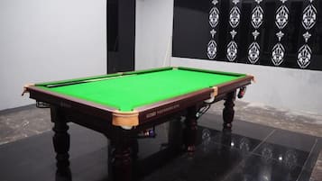 A pool table with a green felt surface, positioned on a glossy black floor.