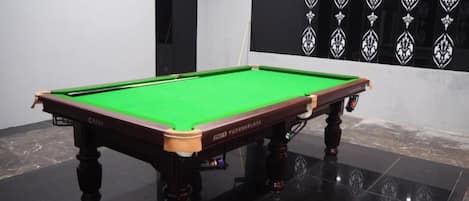 A pool table with a green felt surface, positioned on a glossy black floor.