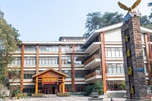 A multi-story hotel with a traditional architectural style, featuring a prominent entrance with a wooden facade and a stone pillar with an eagle sculpture. - Yun Yin Nanshan (Chongqing)