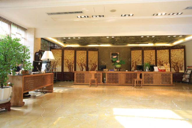 A reception area with a polished marble floor, a wooden reception desk, and a large potted plant.
