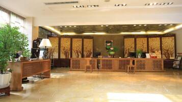 A reception area with a polished marble floor, a wooden reception desk, and a large potted plant.