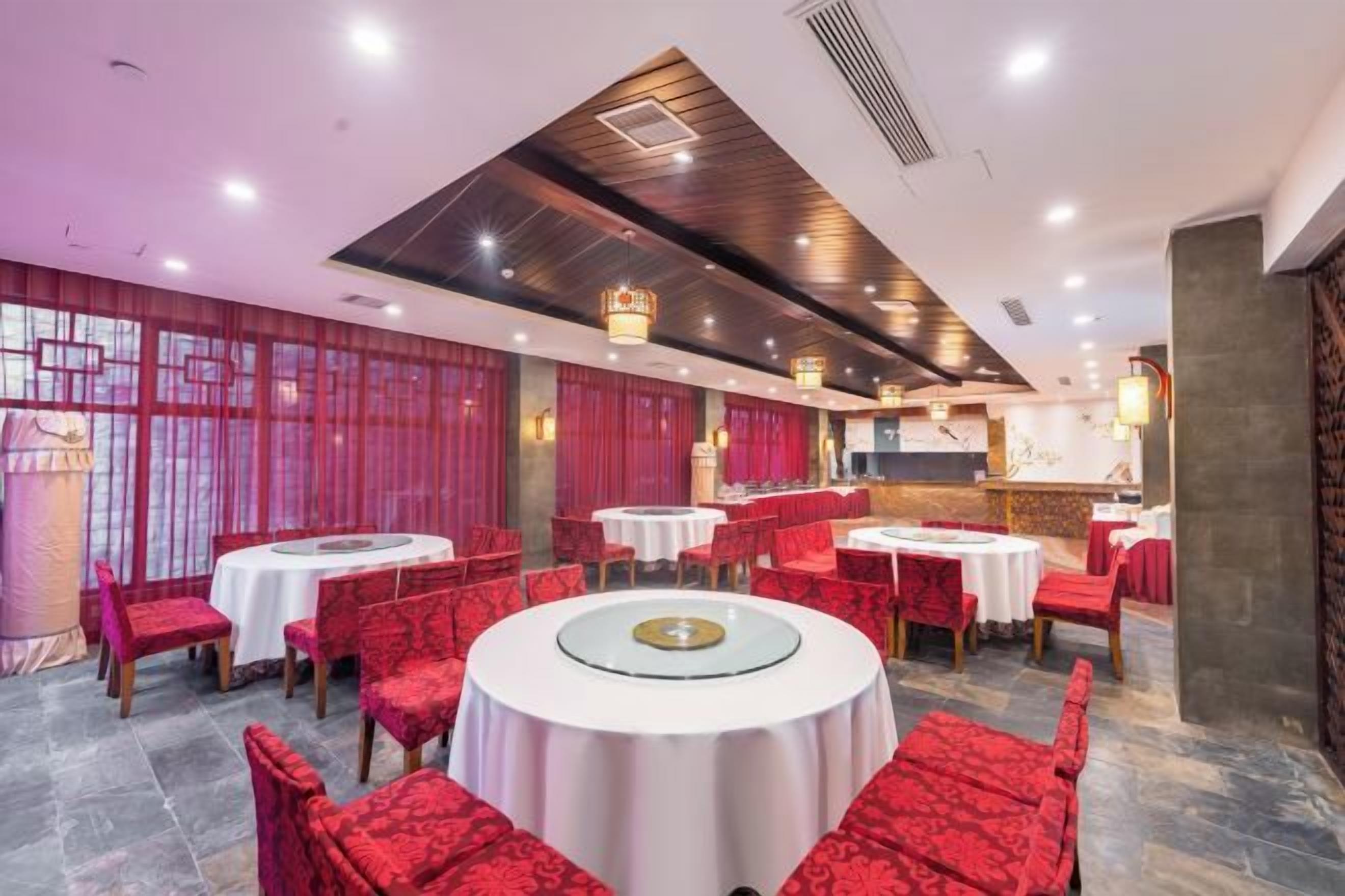 Un restaurant avec des tables rondes et des chaises à revêtement rouge, un coin bar et un plafond décoratif.