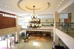 Eine geräumige Lobby mit einem Chandelier, eine Ebene mit Geländer und eine Backsteinwand.