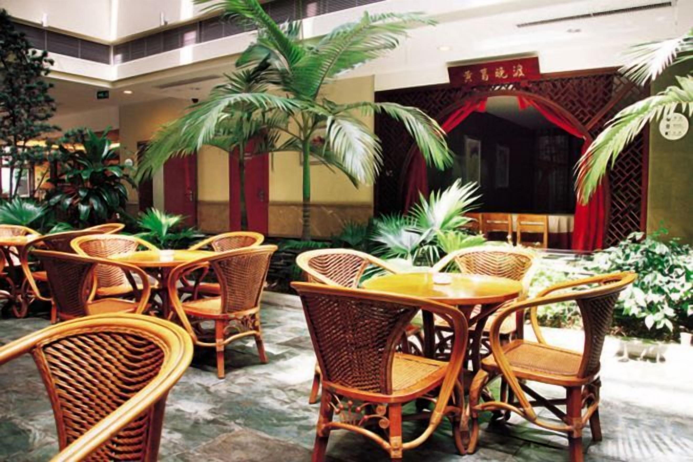 Un hall d’hôtel avec des meubles en osier, des palmiers et une entrée rouge.