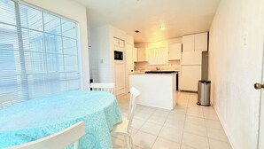 Une cuisine compacte avec des meubles blancs, un petit îlot central et un coin repas comprenant une table et des chaises.