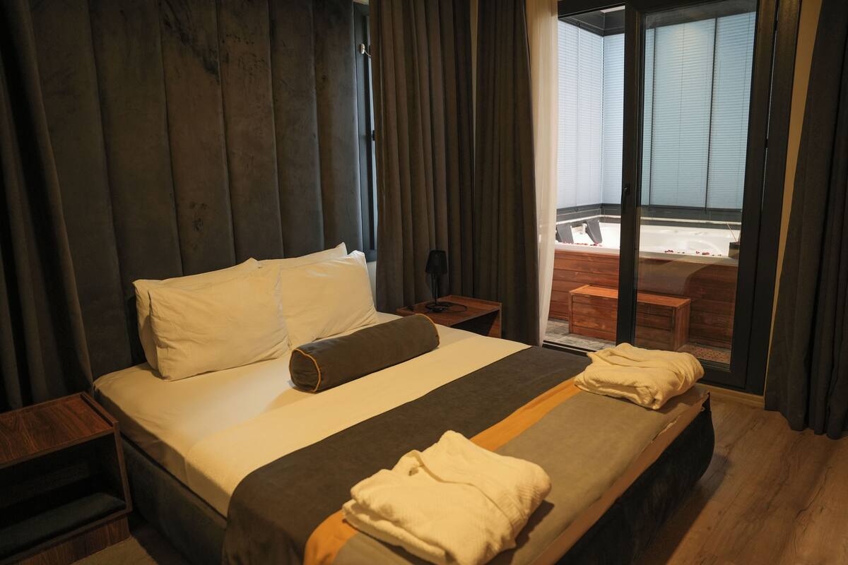 Una camera d'albergo con un letto grande, una testiera di legno, un tavolino e vista su una vasca idromassaggio.