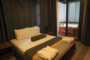 Une chambre dâhĂŽtel avec un grand lit, une tĂȘte de lit en bois, une petite table en bois et une vue sur un jacuzzi.