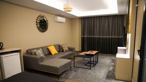 A hotel room with a sofa, a coffee table, a bed, a TV, and a window with curtains. - LIMONOTTO SUIT OTEL (Mersin)