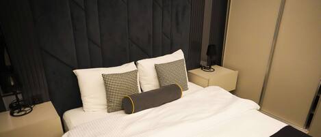 A modern hotel room with a large bed, a black and white checkered pillow, and a black throw blanket with the hotel name.
