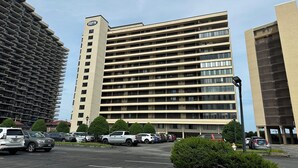 A multi-story hotel with a flat facade, multiple balconies, and a parking lot with various vehicles. - Oceanfront High Point North Studio M8 Just Steps to the Beach! (Ocean City)