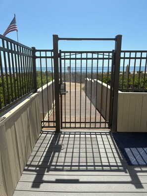 A wooden deck leading to a beach with a metal gate, an American flag, and a clear view of the ocean. - Oceanfront High Point North Studio M8 Just Steps to the Beach! (Ocean City)