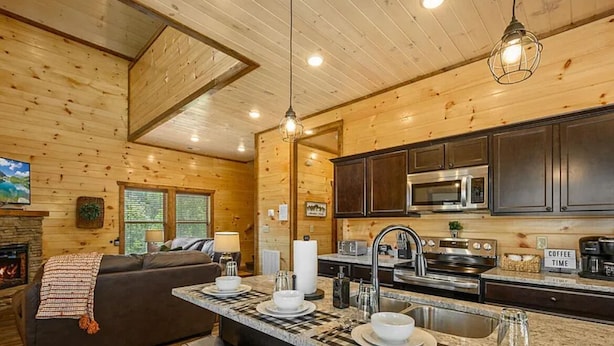 A cozy cabin interior with a wooden interior, a kitchen with a central island, and a fireplace. - Charming Pet Friendly 3 Bedroom Chalet in Pigeon Forge with heated pool (Pigeon Forge)