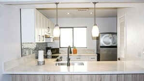 Une cuisine moderne avec des meubles blancs, un réfrigérateur en acier inoxydable, un évier et des luminaires suspendus.