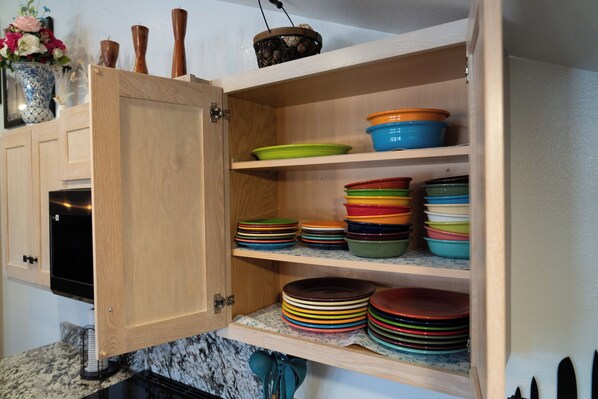 A kitchen cabinet with multiple shelves holding colorful plates and bowls.