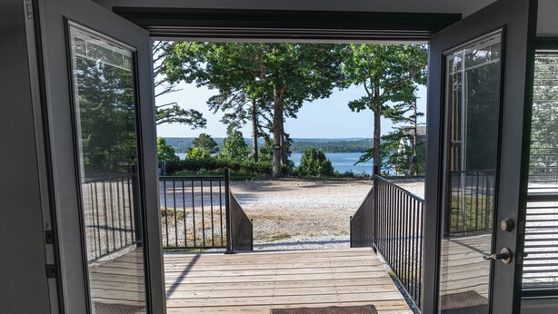 An open door leading to a wooden deck with a view of a lake and trees. - On Beaver Lake! Rogers, AR, NEW Spacious Barndominium With Sweeping Lake Views. (Rogers)