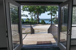 An open door leading to a wooden deck with a view of a lake and trees.