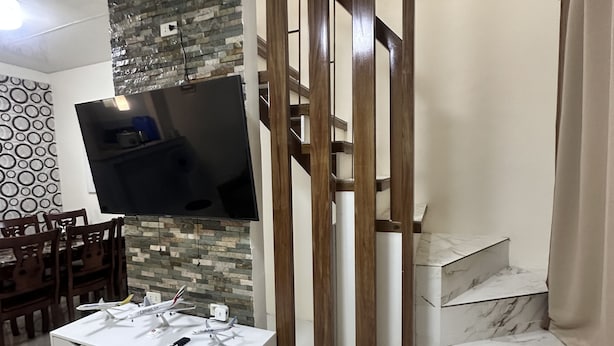 A modern living room with a white entertainment unit, a flat-screen TV mounted on a stone wall, and a staircase with marble steps.